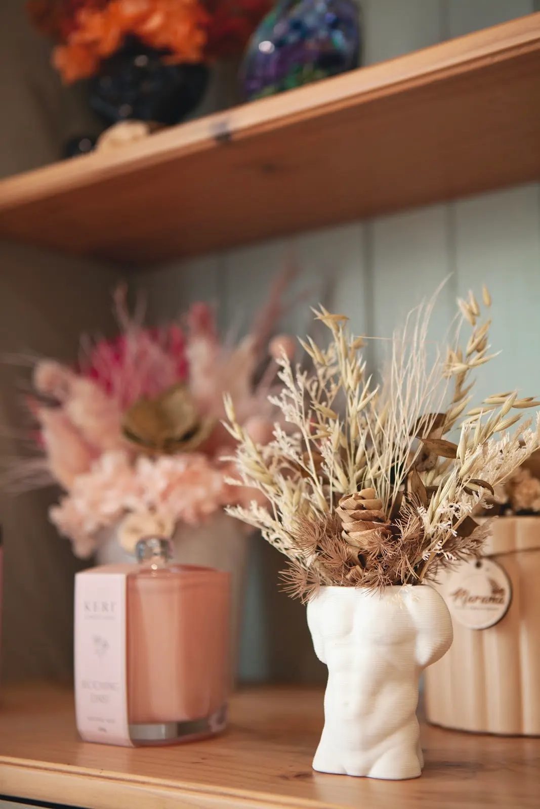 Dried flowers in a white body-shaped vase on a shelf