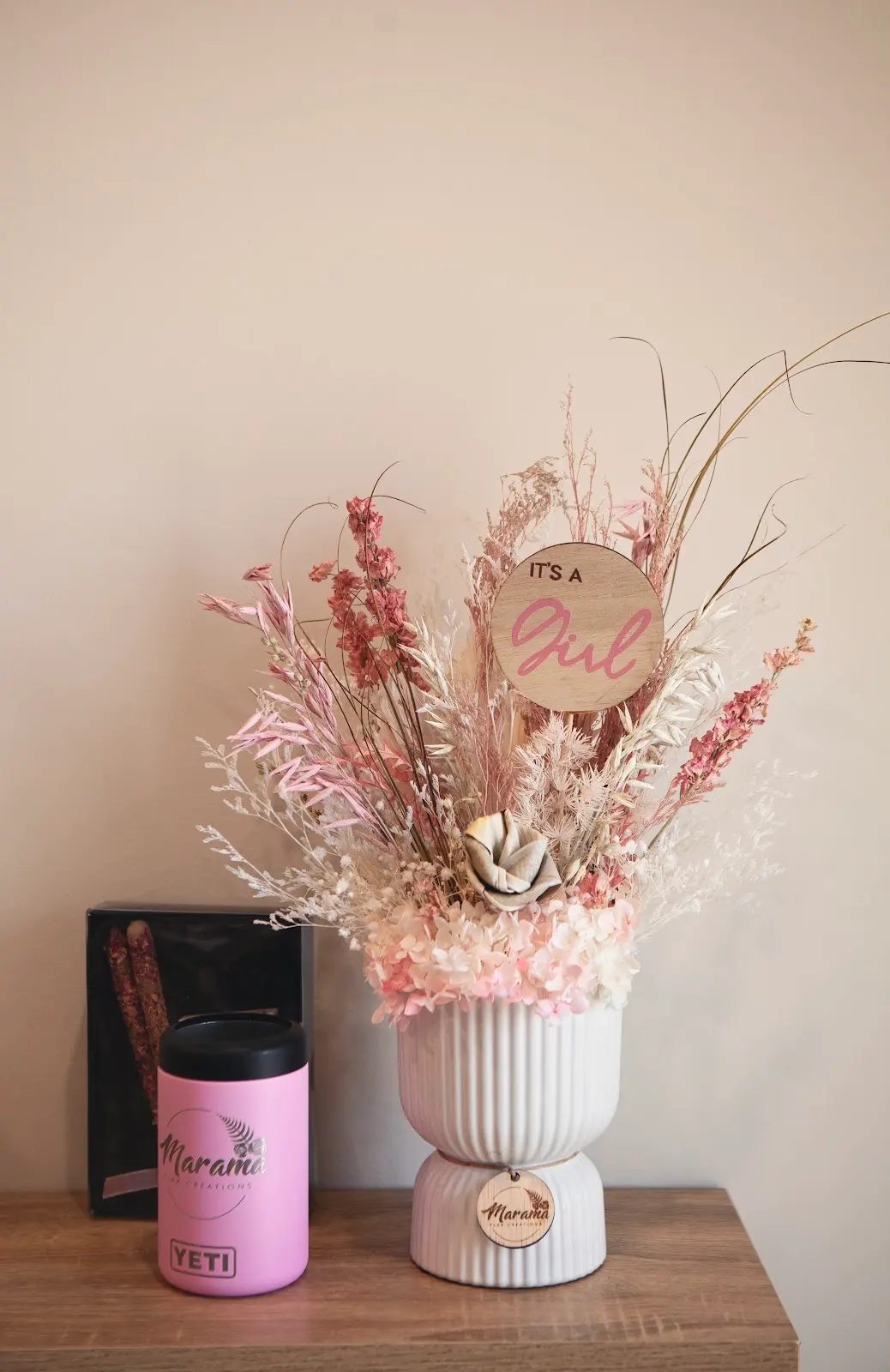 Pink dried flower arrangement in a white ribbed vase with an It's a Girl tag