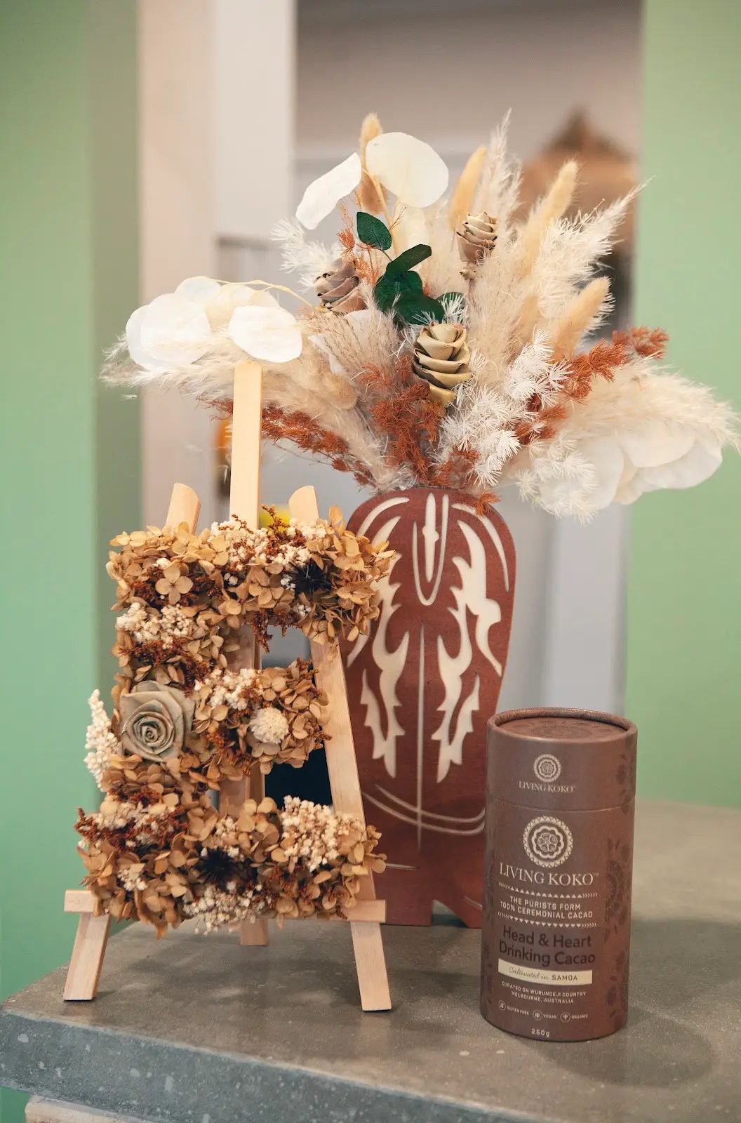 A dried flower letter B on an easel beside a terracotta vase arrangement