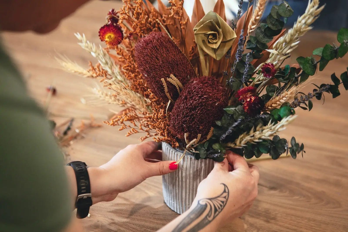Hands holding a rust and mustard dried flower arrangement in a ribbed vase