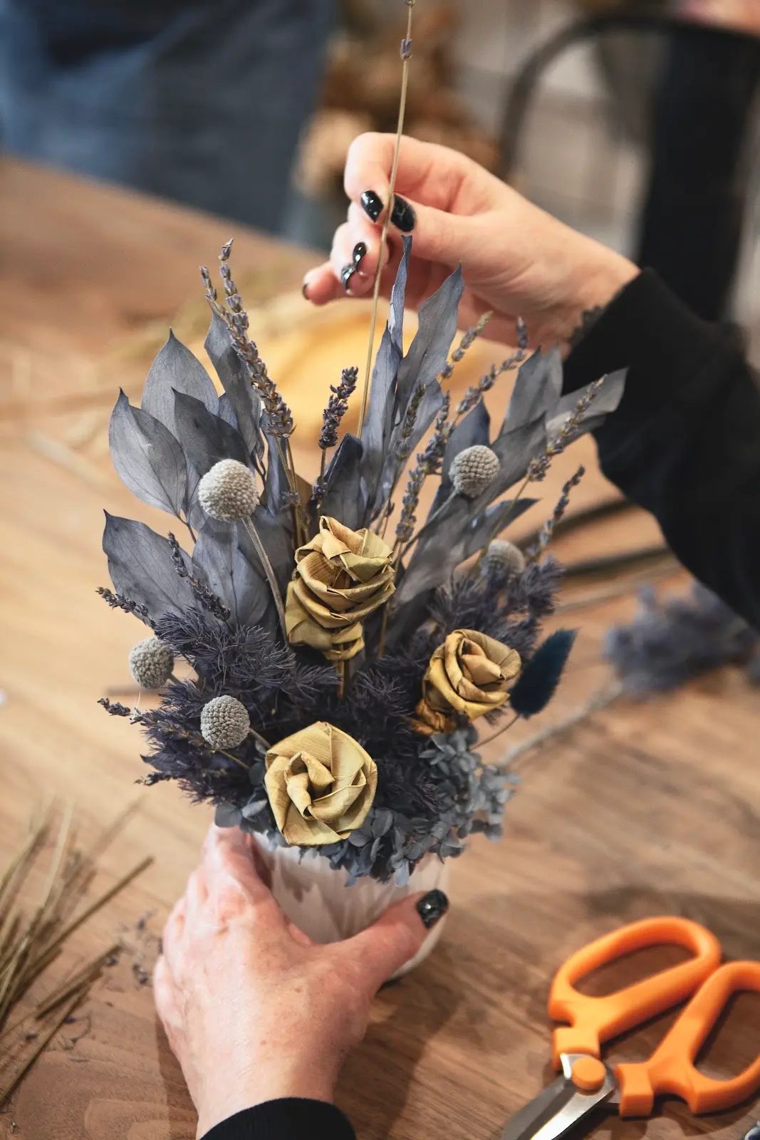 Hands arranging a dusty blue dried flower bunch at a workshop table