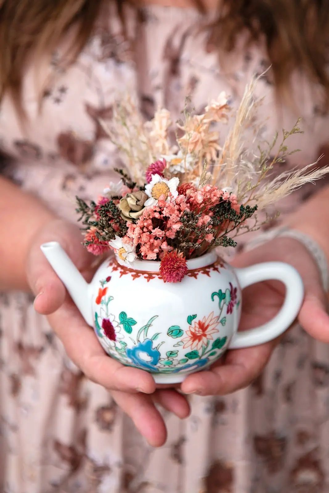 Hands holding a vintage teapot filled with dried flowers