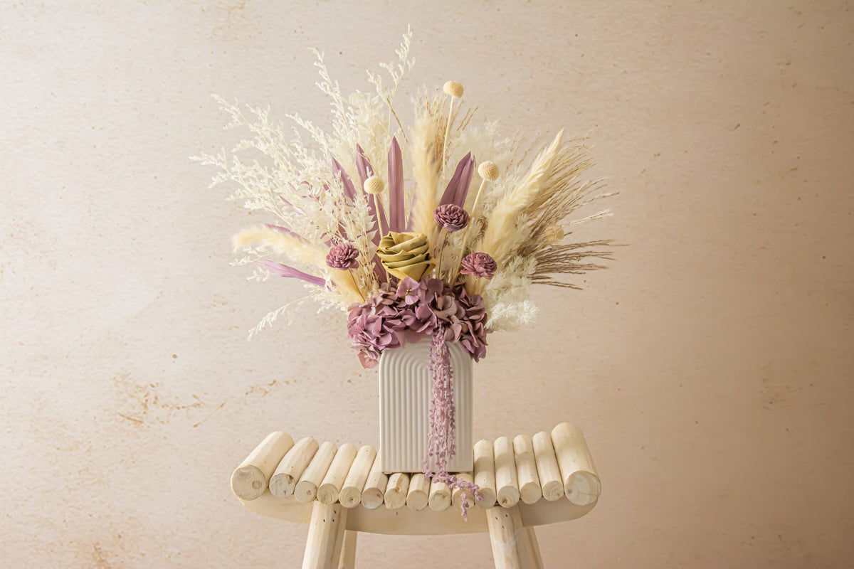 Mauve and cream dried flower arrangement in a ribbed vase on a stool