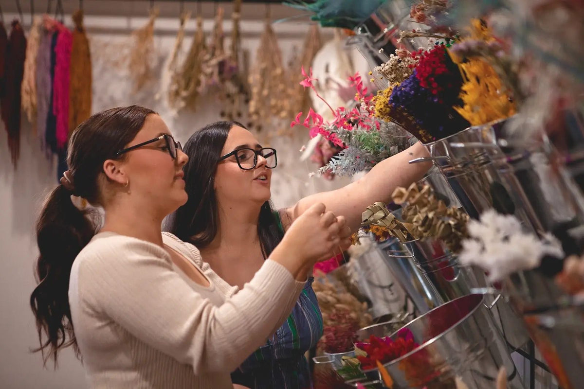 Two women choosing dried stems from the flower wall at the studio